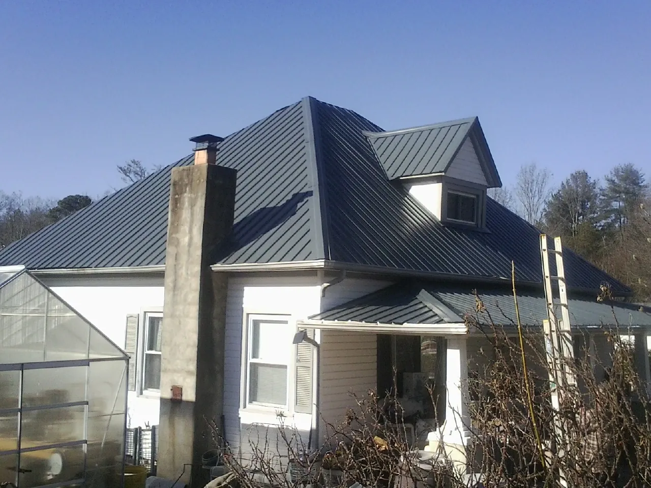 Dark blue standing seam metal roof on a white farmhouse with dormer — Slate & Tile Roof Repair by Roofing Brothers in Harleyville