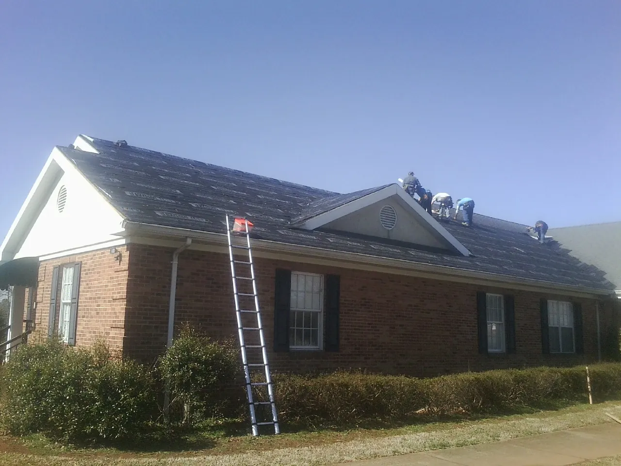 Crew tearing shingles off a brick ranch roof with a ladder set — Emergency Roof Repair work by our crew in Harleyville