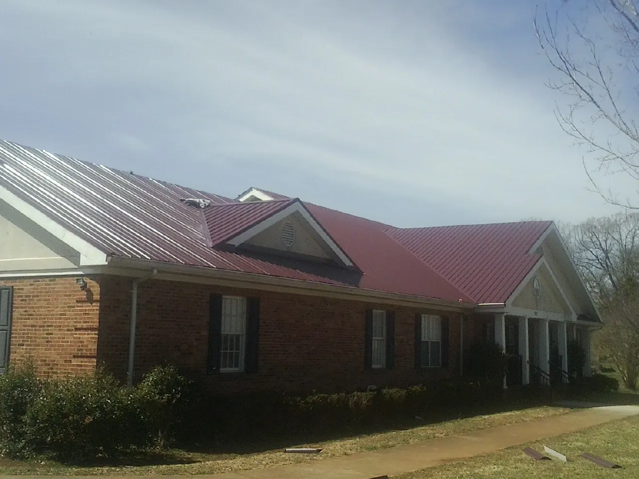 Red metal roof with gabled entries on a long brick building, from a Hail Damage Roof Repair job in Harleyville