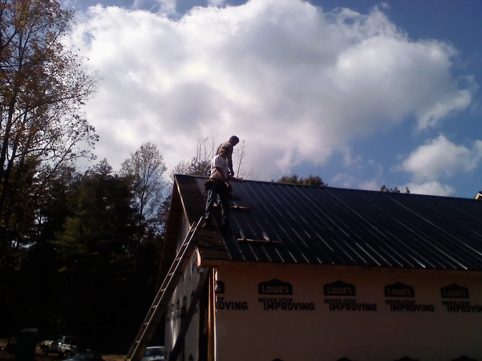 Roofer fastening dark metal panels high against a cloudy sky, from a Roof Inspection job in Harleyville