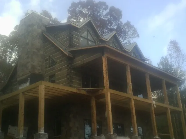 Stone chimney and dormers on a large log home with a timber porch in Harleyville