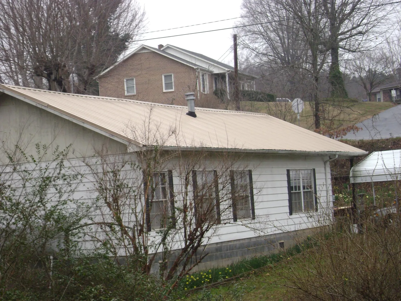 Tan metal roof on a white sided house set into a hillside — Commercial Roofing by Roofing Brothers in Harleyville
